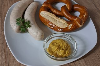 Zwei Weißwürste mit Petersilie, eine Brezel und ein Schälchen mit süßem Senf auf einem weißen, eckigen Teller