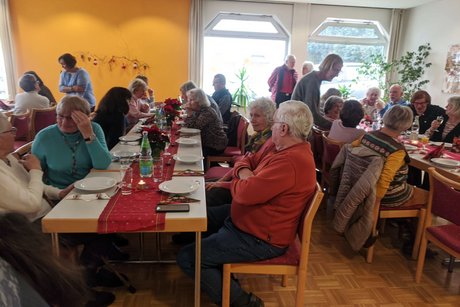 Panoramafoto des Festsaals mit mehreren Tischen, an denen vorwiegend &auml;ltere Menschen sitzen und sich angeregt unterhalten