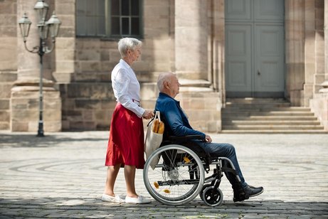 Eine ältere Frau schiebt ihren Mann im Rollstuhl