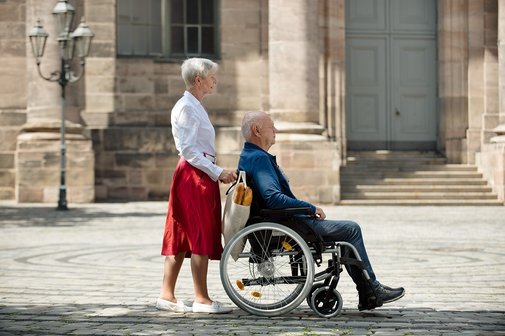 Eine ältere Frau schiebt ihren Mann im Rollstuhl