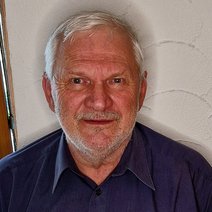 Gunter Seeger l&auml;chelnd mit einem blauem Poloshirt, vor einer wei&szlig;en Wand.