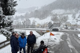 Auf der Ortsquerstraße Mitte auf der linken Seite von Schlechtnau wieseabwärts gesehen. Bei winterlicher Witterung: Ortsvorsteher und Kreisrat Sven Behringer, Baudirektor beim Regierungspräsidium Oliver Gassenmeier, Kreisrat Eduard Behringer, Ortsvorsitzender Oberes Wiesental BÜNDNIS 90/DIE GRÜNEN Hartmut Schwäbl, Rollstuhlfahrerin, Schriftführerin des VdK Ortsverbands Karin Maier mit Behindertenbegleithund, Foto von links. Es fehlt die Abgeordnete Sarah Hagmann (MdL