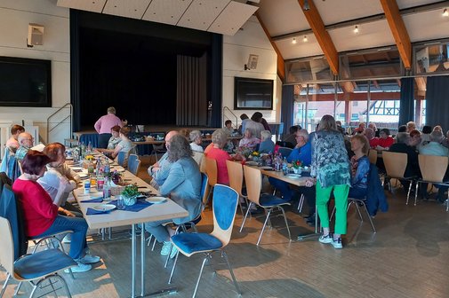Teilnehmer der Hauptversammlung sitzen an langen Tischen und unterhalten sich.
