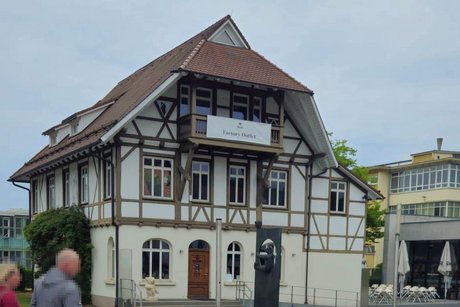Dreistöckiges Fachwerkhaus mit Balkon im obersten Stockwerk, an dem ein Banner mit der Aufschrift „Factory Outlet“ hängt.