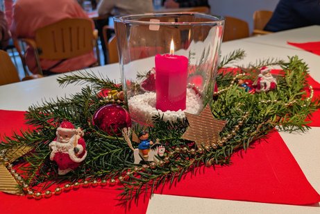Tischdekoration mit roten Servietten, Tannenzweig als weihnachtlicher Schmuck, Christbaumanh&auml;nger auf dem Zweig und einer brennenden Kerze in einem transparenten Glasgef&auml;&szlig;.