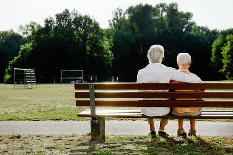 Rückenansicht eines weißhaarigen Mannes und einer weißhaarigen Frau auf einer Bank sitzend im Park