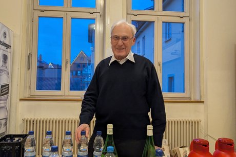 Ein älterer Mann steht vor einem Tisch, auf dem mehrere 0,5-Liter-Plastikflaschen mit Sprudelwasser stehen.