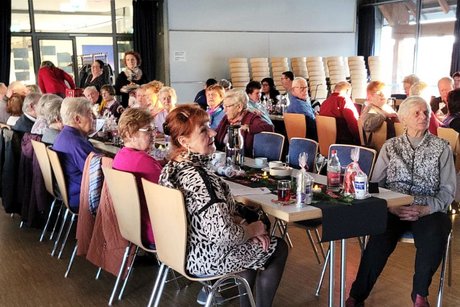 Tischreihe, an der mehrere ältere Menschen sitzen und aufmerksam dem Orchester zuhören.