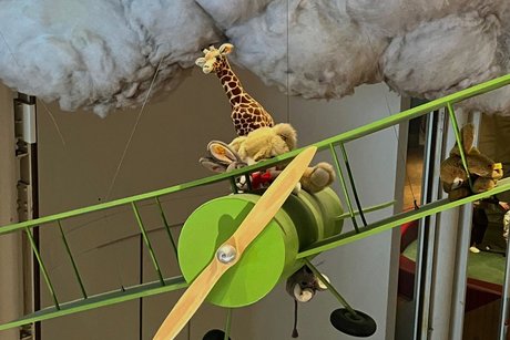 Modell eines Doppeldeckerflugzeugs, in dem ein Hase, ein Teddybär und eine Giraffe sitzen, darüber eine große Wattewolke