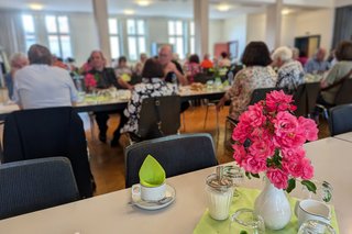 Weiße Blumenvase mit rosa Blümen auf einem Tisch. Hintergrund mit Personen an Tischen verschwommen