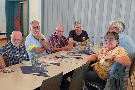 Sechs Personen sitzen an einem Tisch, wirken ausgelassen und l&auml;cheln fr&ouml;hlich in die Kamera.