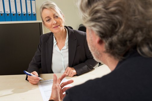 Eine Juristin, die einen Stift in der Hand hält und ein Schreiben vor sich liegen hat, berät einen Mann im Sozialrecht