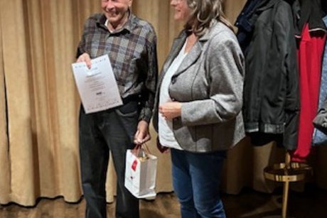 Jahresabschlussfeier VdK-OV Aichwald 2025 Frau im Jacket mit Geschenktasche steht neben einem älteren Mann, der eine Urkunde hält.