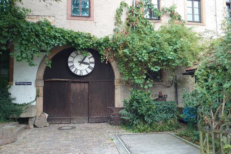 altes Scheunentor mit gro&szlig;en Uhrenzifferblatt umrankt von Efeu im Hof des Winzermuseums Rauenbergg