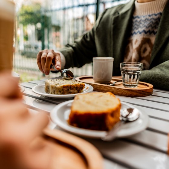 Nahaufnahme einer Frau, die mit Freunden Kuchen isst und Kaffee trinkt.