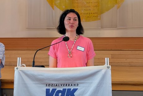Mittelalte Frau mit lachsfarbener Bluse und schwarzen, mittellangen Haaren am Rednerpult.