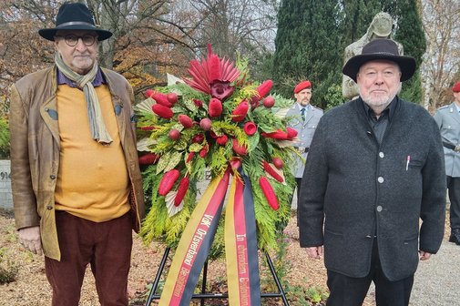 Benno Belzhuber und Karl Reichert stehen neben einem Kranzgebinde vor einem Ehrenmal