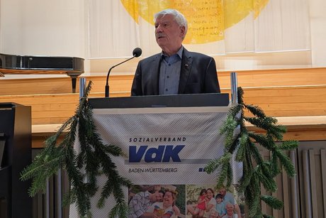 Vorweihnachtlicher Nachmittag Mann mit grauen Haaren und Schnauzbart, Hemd und Sakko, steht an einem Rednerpult.