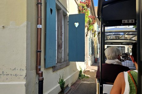 Der kleine Zug f&auml;hrt dicht an den H&auml;userfasaden entlang, ein himmelblauer Fensterladen mit einem ausges&auml;gten Herzchen steht am Haus ab.