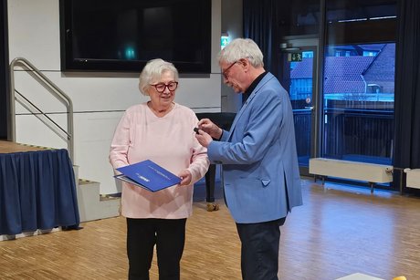 Hauptversammlung VdK OV Echterdingen 2026 Ein älterer Herr im Jacket überreicht ein Schmucketui an die Dame links von ihm, die bereits eine Urkunde hält