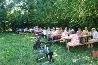 Mitglieder und Gäste des VdK sitzen an Biertischen beim Grillfest im Garten des Rauenberger Winzermuseums.