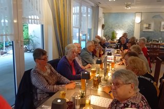 Bild zeigt eine lange Tafel mit Frauen und Männern mit Getränken auf den Tisch