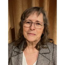 Frau mit Brille l&auml;chelt charmant in die Kamera und tr&auml;gt ein graues Jackett.