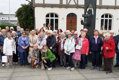 Gruppenbild mit etwa 40 älteren Menschen vor einem gusseisernen Denkmal mit einem Teddybär.