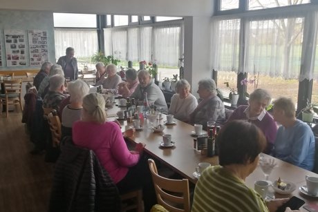 Karin Koletzko und eine größere Runde von Teilnehmenden (am Fensterplatz) in vertieften Gesprächen Das Bild zeigt Karin Koletzko und eine größere Runde von Teilnehmenden (am Fensterplatz sitzend) in vertieften Gesprächen
