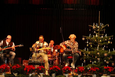 Band "Just 4 fun" mit Gitarren, im Hintergrund das Schlagzeug auf der B&uuml;hne der Kulturhalle. Im Vordergrund rote Weihnachtssterne als Abgrenzung der B&uuml;hne. Rechts ein mit Sternen dekorierter Christbaum