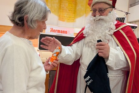 Ein Mann im Nikolauskostüm überreicht einer Frau einen Schokonikolaus.