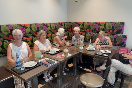Es sitzen ein paar Leute bei Kaffee und Kuchen an einem Tisch und unterhalten sich.