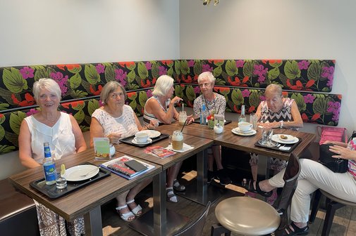 Es sitzen ein paar Leute bei Kaffee und Kuchen an einem Tisch und unterhalten sich.