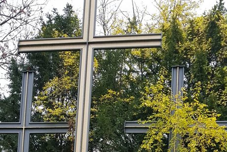 Drei mehrere Meter hohe Kreuze, von denen nur die oberen Teile sichtbar sind. Ein Kreuz wird teilweise von einem Baum verdeckt.