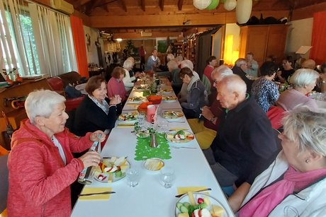 Sommerausflug VdK OV RSKN-Esslingen 2025 Langer Tisch mit mehreren älteren Menschen, vor jedem Teller mit Käsekostproben und Brotkörben in der Mitte, während sie sich unterhalten.
