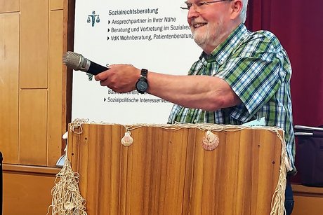 Ladi unser Moderator Vorsitzender und Moderator Ladi Toth am Rednerpult mit Mikrofon in der Hand.