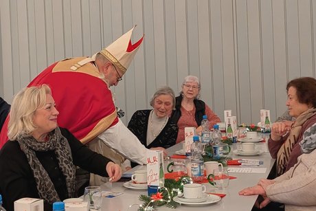 Vorweihnachtlicher Nachmittag Nikolaus beugt sich vor und reicht einer älteren Dame Süßigkeiten.