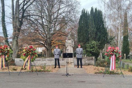 Zwei Soldaten in Ausgehuniform halten Wache an einem steinernen Ehrenmal für ihre toten Kameraden. Zwei Kränze links davon. Einer rechts. Alles sehr würdevoll.