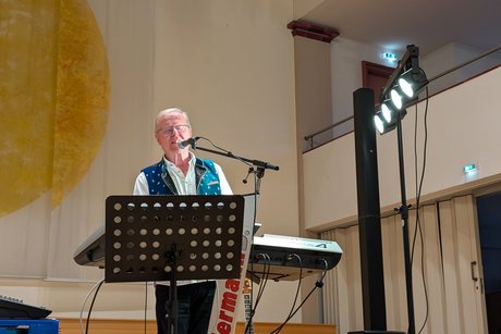Mann auf der Bühne, vor ihm ein Keyboard und ein Mikrofon, in das er singt.