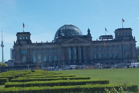 Das Reichstagsgeb&auml;ude mit drei wehenden Fahnen und gr&uuml;nen Hecken im Vordergrund