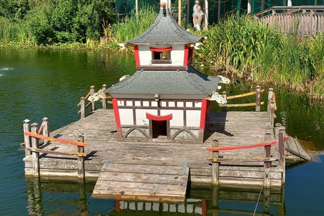 Kleine, modellhafte Nachbildung eines japanischen Tempels auf einer Holzinsel in einem Teich.
