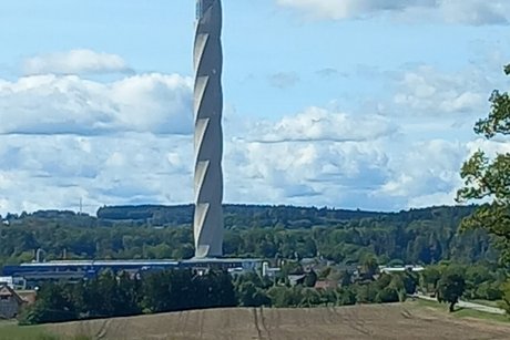 Blick aus dem fahrenden Bus auf einen schlanken, hohen Turm in Form eines Bohrers.