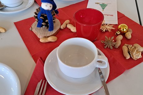 weihnachtliche Tischdeko: blaues Tannenzapfenm&auml;nnchen, Teelichte in rotem Glas, Weichnachtsschmuck, Erdn&uuml;sse und Kaffeegeschirr