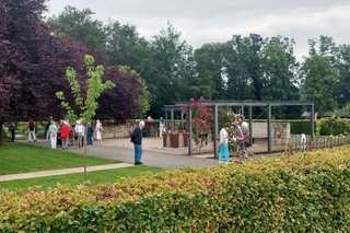 Ein Landschaftspark mit Bäumen und Hecken, durch den Personen spazieren.