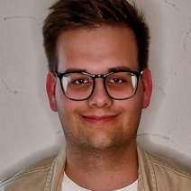 Sebastian Nietsch l&auml;chelnd mit einer beige Hemdjacke und wei&szlig;em T-Shirt, vor einer wei&szlig;en Wand.