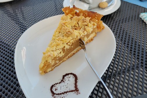 Bild zeigt einen Kuchen auf Herzteller. Im Hintergrund eine Tasse Kaffee.