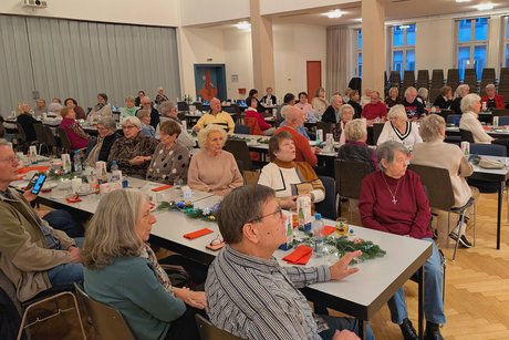 Vorweihnachtlicher Nachmittag Festsaal mit vielen Menschen, die an Tischen sitzen und singen.