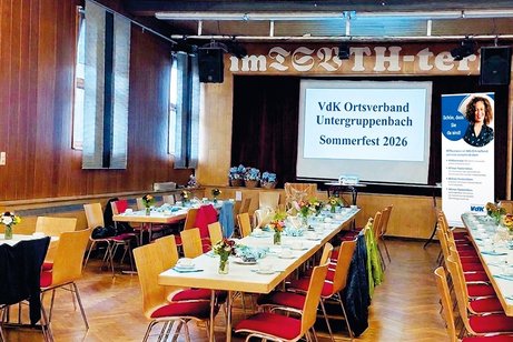 Ansicht auf noch leeren aber schon dekorierten Saal. Lage Tischreihen im Hintergrund Leinwand mit Mit Text und rechts Roll up des Ortsverbandes