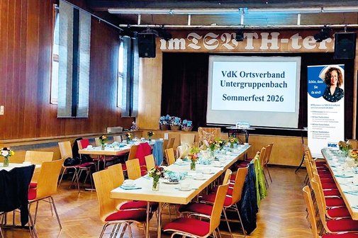 Ansicht auf noch leeren aber schon dekorierten Saal. Lage Tischreihen im Hintergrund Leinwand mit Mit Text und rechts Roll up des Ortsverbandes