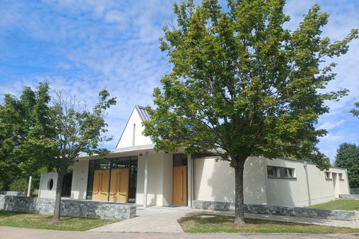 Die neue wei&szlig;e Aussegungshalle mit gr&uuml;nen B&auml;umen davor und einem blauen Himmel